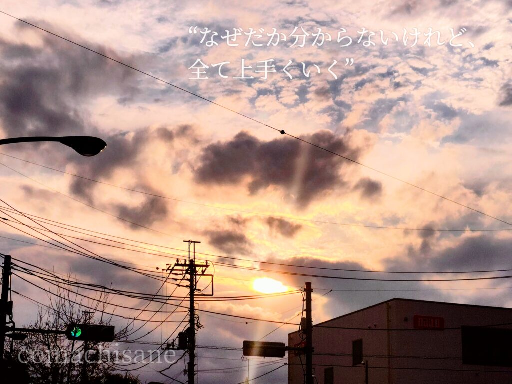 雲間から夕陽の光がこぼれる幻想的な街中の空と「なぜだか分からないけれど全て上手くいくという」アファメーション